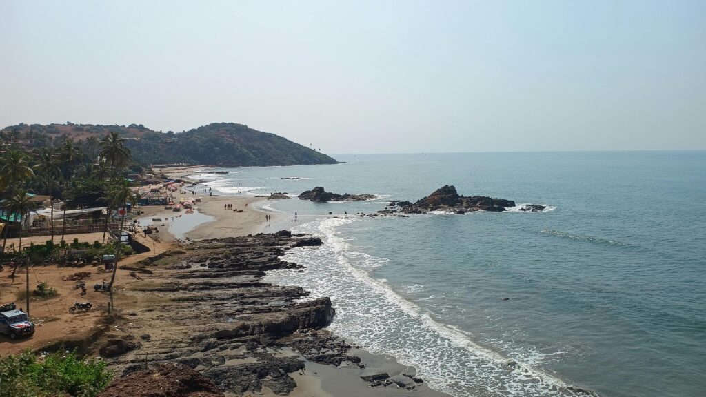 Explore the serene Anjuna Beach in Goa, showcasing beautiful sandy shores and rocky coastline. Budget travel in Goa