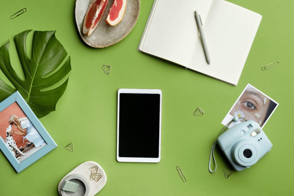 A flat lay featuring stationery, a camera, and a tablet on a green background, perfect for creative concepts, social media content planning
